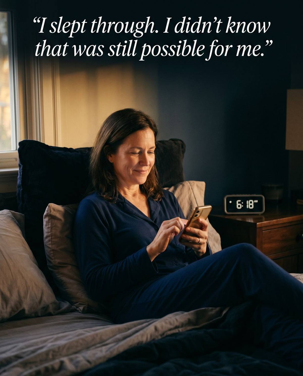 Woman in navy pajamas sitting up in bed at 6:18 AM, smiling at her phone in morning light — I slept through. I didn't know that was still possible for me.